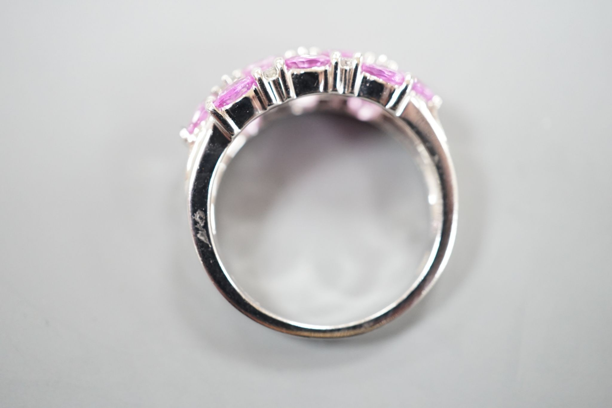 A modern 14k white metal, pink sapphire and diamond cluster set half hoop dress ring, size O, gross weight 4.6 grams.